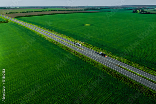 two fuel trucks wr on the higthway at sunset. cargo delivery driving on asphalt road among the green fields with goods. seen from the air. Aerial view landscape. drone photography. convoys with cargo