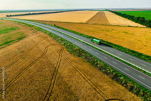 green truck on the higthway among the wheat fields. cargo delivery driving on asphalt road seen from the air. Aerial view landscape. drone photography. © drotik