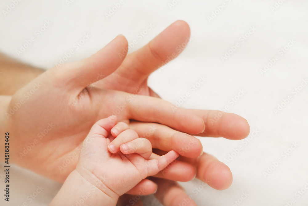 Newborn Baby Hand In Mother and Father Hands on White Blanket. Concept of Parenthood And Happy Family. Mom, Dad and their Child. Newborn Baby Hand In Mother and Father Hands on White Blanket. Concept of Parenthood And Happy Family. Mom, Dad and their Child.