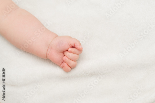 Palm In Fist Of Newborn Baby On White Blanket. Text Space. Child Protection or Adoption