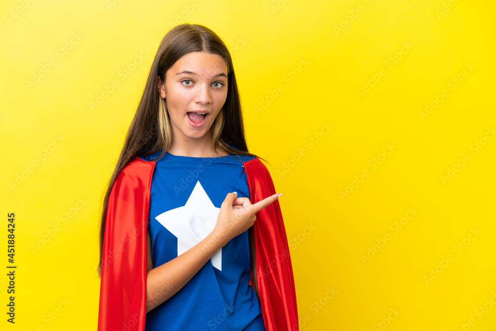 Little caucasian superhero girl isolated on yellow background surprised and pointing side Little caucasian superhero girl isolated on yellow background surprised and pointing side