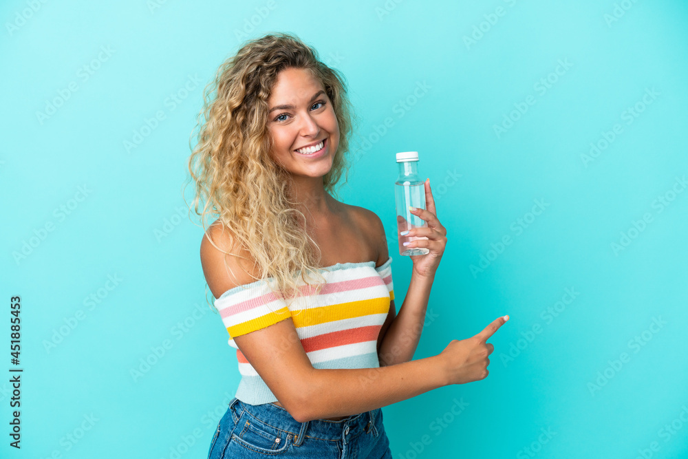 Young blonde woman with a bottle of water isolated on blue background pointing back Young blonde woman with a bottle of water isolated on blue background pointing back