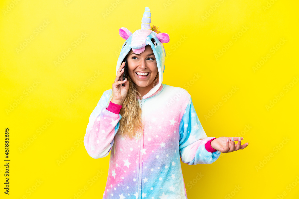 Girl with curly hair wearing a unicorn pajama isolated on yellow background keeping a conversation with the mobile phone with someone Girl with curly hair wearing a unicorn pajama isolated on yellow background keeping a conversation with the mobile phone with someone