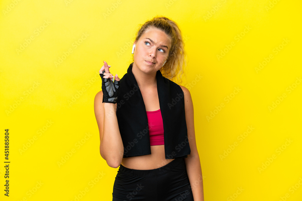 Sport woman with towel isolated on yellow background with fingers crossing and wishing the best Sport woman with towel isolated on yellow background with fingers crossing and wishing the best