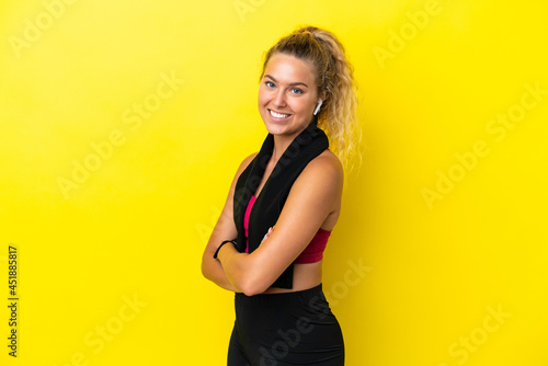 Sport woman with towel isolated on yellow background with arms crossed and looking forward