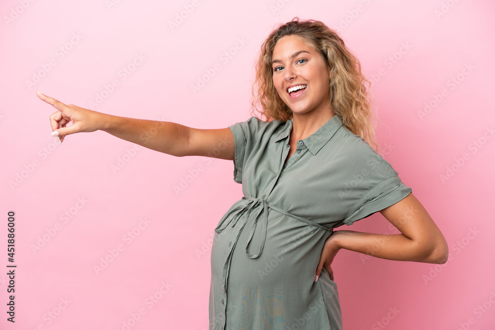 Girl with curly hair isolated on pink background pregnant and pointing to the lateral Girl with curly hair isolated on pink background pregnant and pointing to the lateral