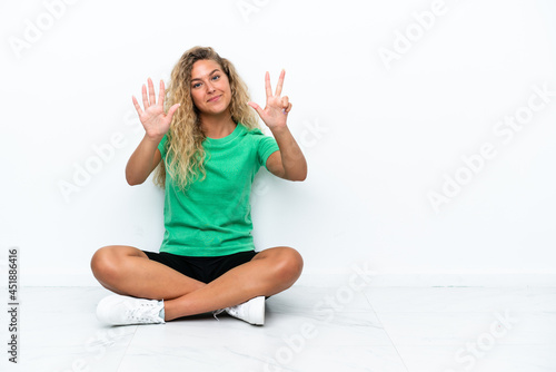 Girl with curly hair sitting on the floor counting eight with fingers