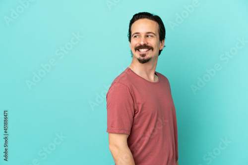 Young caucasian man isolated on blue background looking to the side and smiling