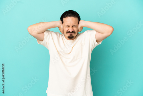 Young caucasian man isolated on blue background frustrated and covering ears