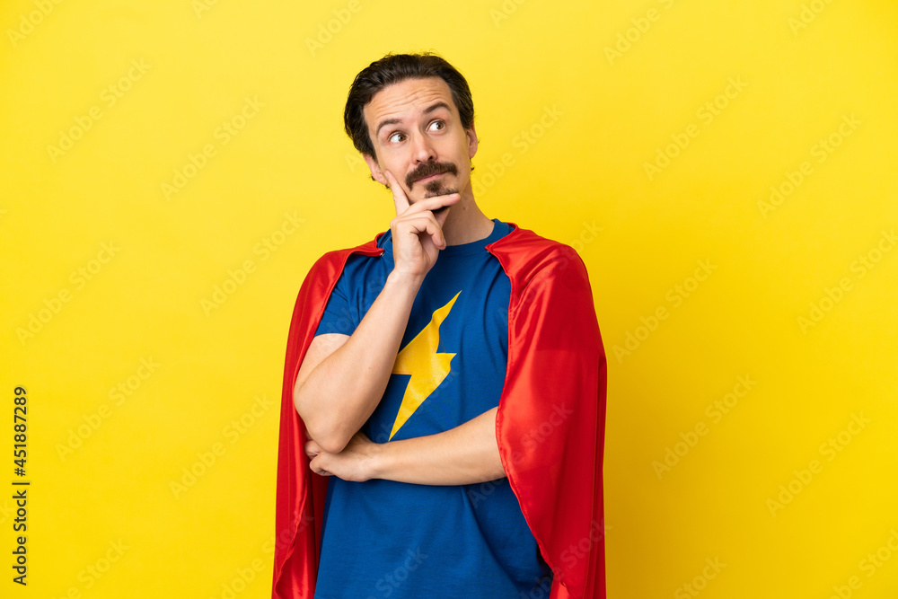 Young caucasian man isolated on yellow background in superhero costume and thinking Young caucasian man isolated on yellow background in superhero costume and thinking