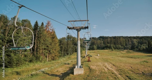 A peaceful sunset over a ski lift, capturing the quiet beauty of an off-season mountain resort. The golden light illuminates the chairlift and surrounding landscape, evoking calmness. photo