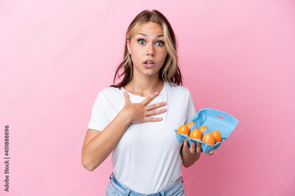 Young Russian woman holding eggs isolated on pink background surprised and shocked while looking right Young Russian woman holding eggs isolated on pink background surprised and shocked while looking right