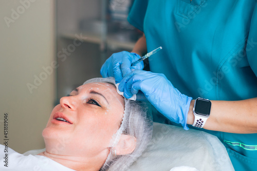  Botox injection into horizontal mimic wrinkles on the forehead by a master in a cosmetology office. Disinfection of the face before the procedure