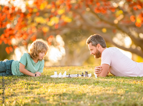 happy family of daddy and son kid playing chess on green grass in park outdoor, genius