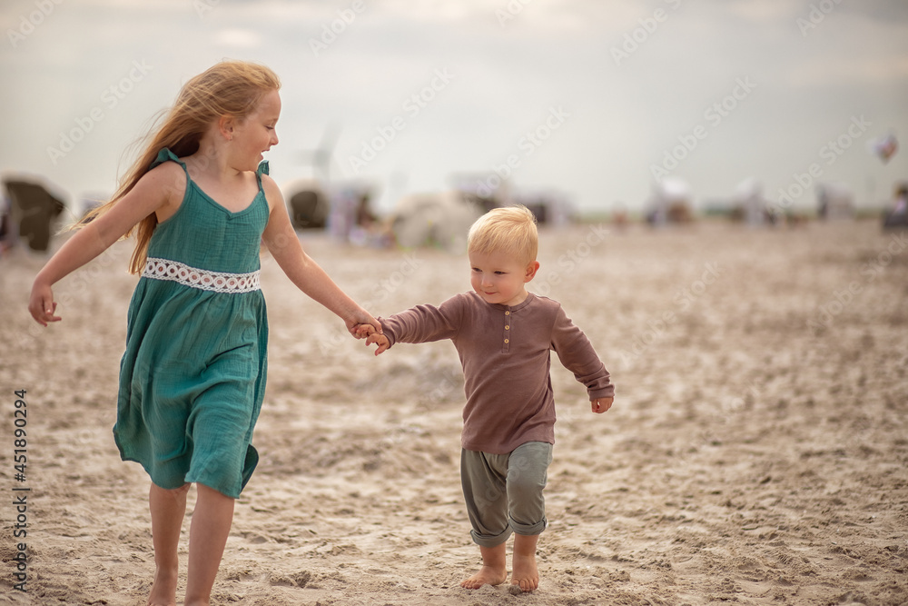 little boy and girl run in the summer along the seashore, holding hands. Brother and sister in natural clothes. Tourism, vacations, traveling with children, sun protection and safety.