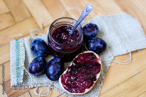 A piece of bread spread with plum jam and a glass jar on retro background. Healthy food background concept. Close up, selective focus and copy space