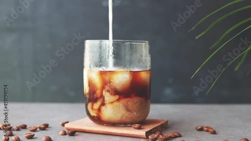 Milk cream is poured into a iced coffee. Coffee cold drink with ice and milk.