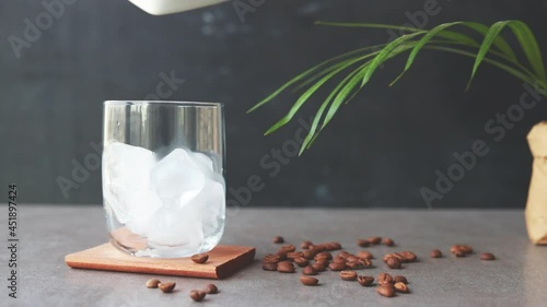 Pouring coffee on ice cubes in glass.