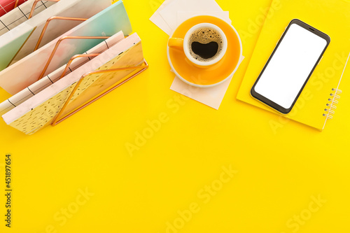 Mobile phone with notebooks and cup of coffee on color background