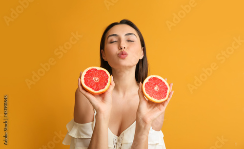 Young woman with juicy grapefruit on color background