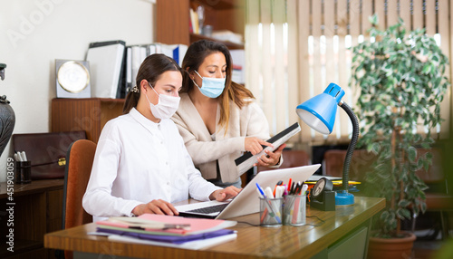 Portrait of two business woman in protective face masks chatting about work in office