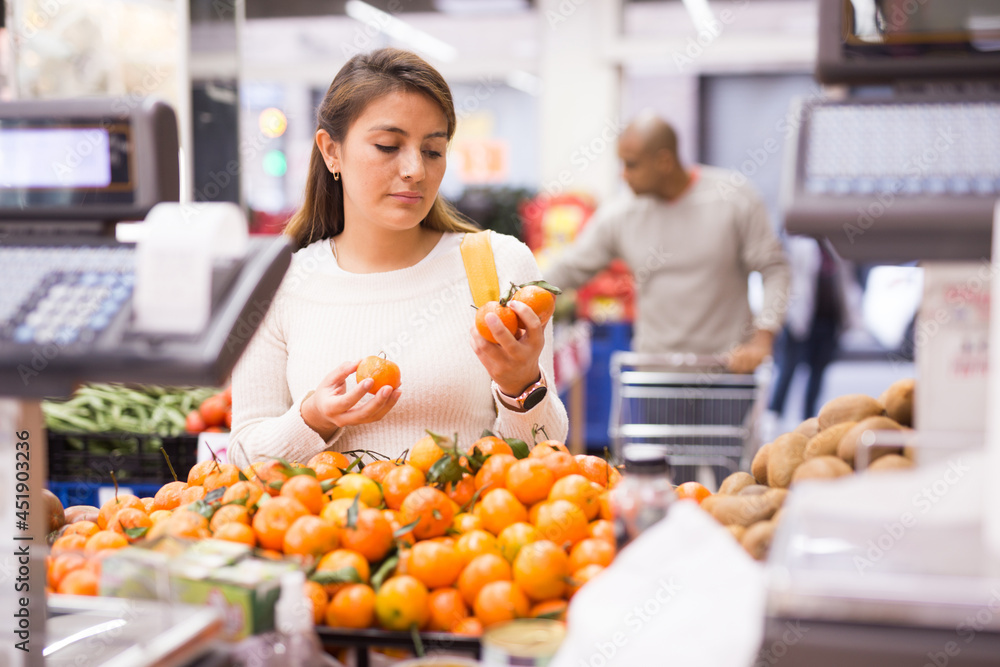 Portrait of latin american woman choosing ripe tangerines in supermarket near till