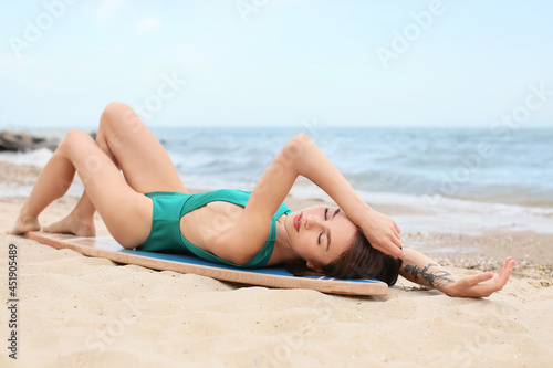 Beautiful young woman with surfboard on beach at resort