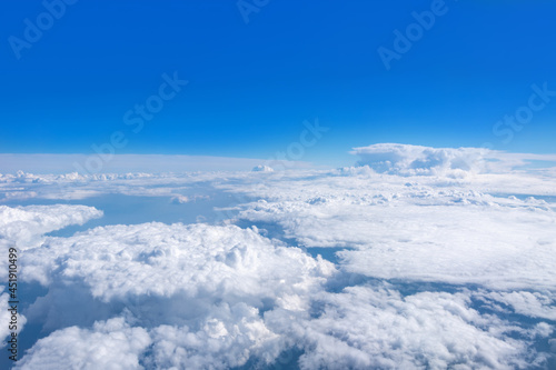 Top view from the airplane window on beautiful cumulus fluffy white clouds on a blue sky with a bright sun. Perfect abstract sky background, wallpaper, layout.