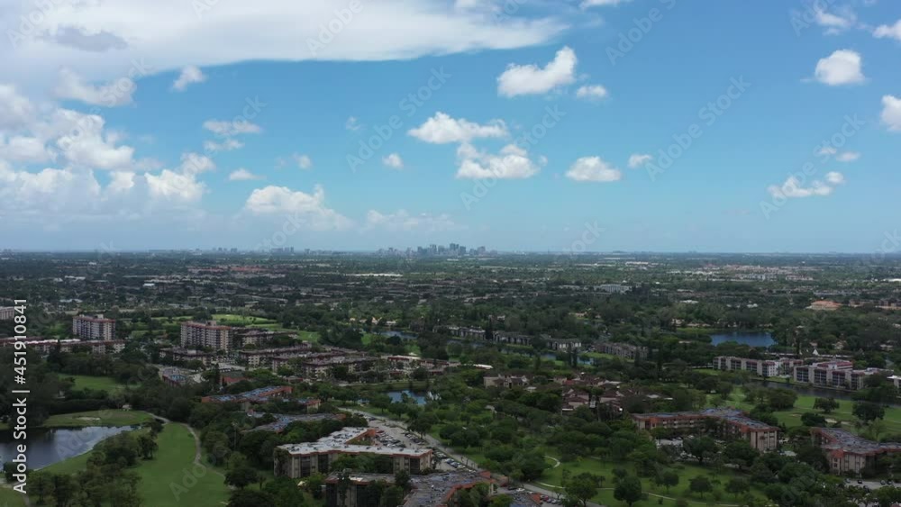 An aerial view of green trees and grass on a sunny day over apartment buildings. The camera dolly in and boom down towards the trees, there are clouds above and more apartments in the distance. An aerial view of green trees and grass on a sunny day over apartment buildings. The camera dolly in and boom down towards the trees, there are clouds above and more apartments in the distance.