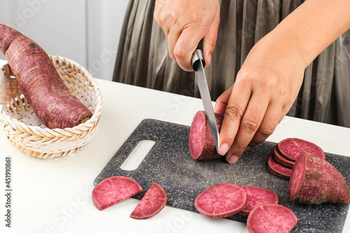 Selected Focus A Woman Slice Cut Japanese Purple Sweet Potato with Knife in the Kitchen, White Background, Kitchen Process Concept photo