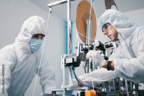 Two scientists wearing uniform protection. Check the manufacturing process face masks. With machinery in a laboratory at industry plants. The concept for security and protection coronavirus covid-19.