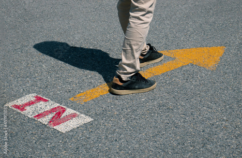 Feet and arrow on asphalt road background in starting line beginning idea.