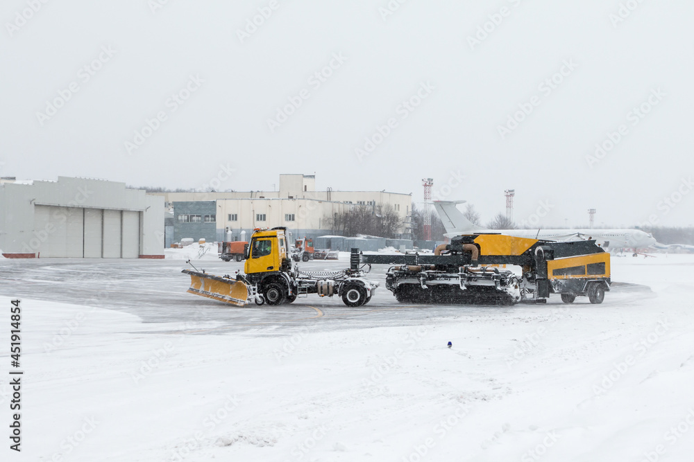 Airfield snow blowers cleaning the area near the airplane hangar at the airport in a severe blizzard