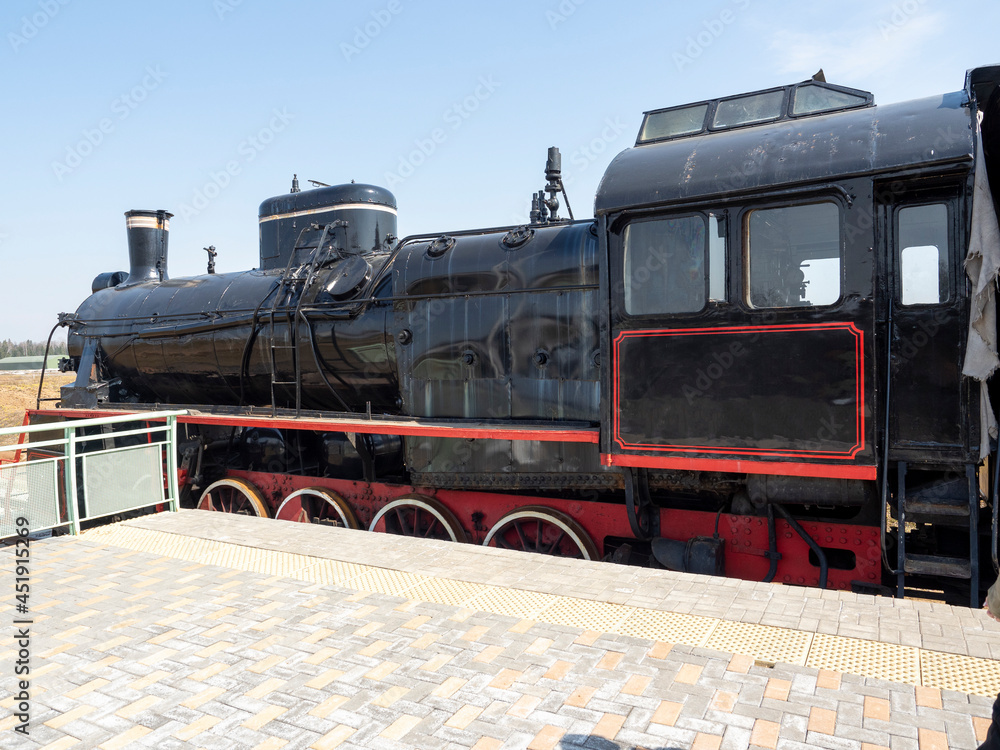 An old vintage black steam locomotive is standing on the platform. Old technologies