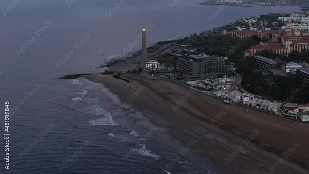 Aerial shot of Maspalomas Lighthouse with light in the evening. Drone view of a city by the sea surrounded by sandy beach in Gran Canaria island Maspalomas in Spain.