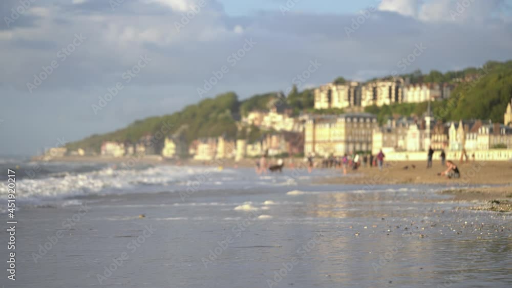 Tourists On Sandy Shore Of Beach With A View Of Waterfront Hotels In Background In Trouville, France. - wide shot Tourists On Sandy Shore Of Beach With A View Of Waterfront Hotels In Background In Trouville, France. - wide shot