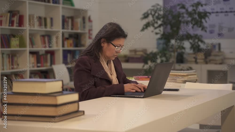 Close up shot of middle aged woman wit glasses typing on laptop in library Close up shot of middle aged woman wit glasses typing on laptop in library