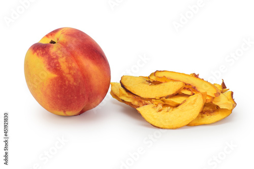A whole ripe nectarine next to a pile of dried slices of this fruit on a white background