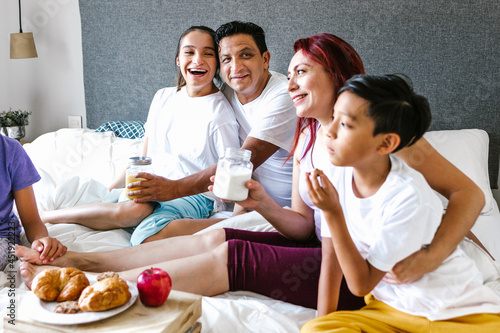 Hispanic teenage girl with cerebral palsy and her family having breakfast on bed at home, in disability concept in Latin America photo