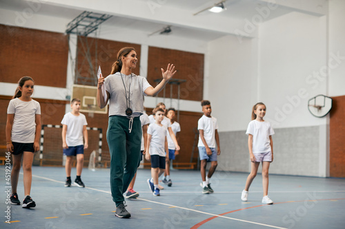 Young female coach has PE class with group of elementary students at school gym. photo