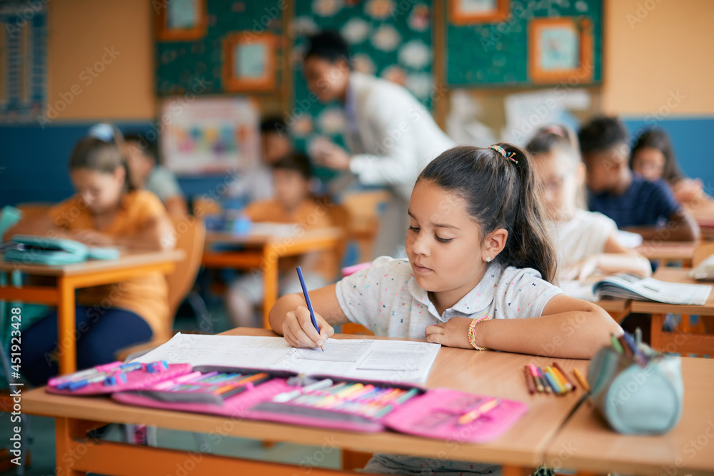 Fototapeta premium Little girl writes in notebook while having class at elementary school.