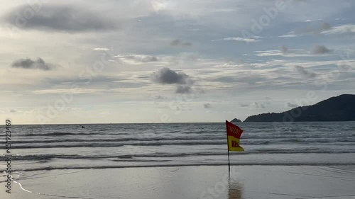 Tropical beach, sea, waves, tourists resting. Water scooter, jet ski moving along the surface of the water. Red yellow lifeguard flag allows people from swimming. Cloudy sky. Sunset. Thailand. Phuket  photo