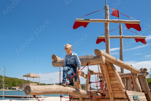 A boy is playing on a wooden playground in the form of a ship. Afternoon walk. Selective focus.