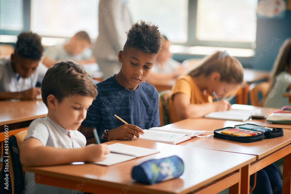 African American schoolboy and his classmates write during class in classroom. African American schoolboy and his classmates write during class in classroom.