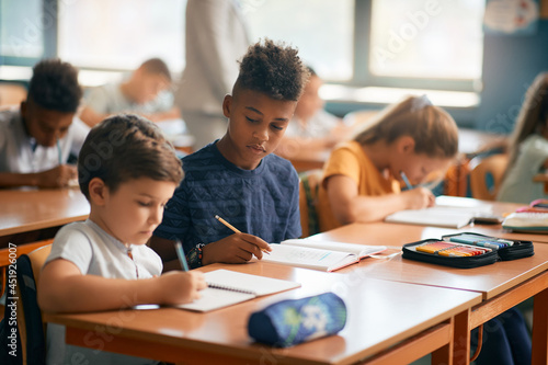 African American schoolboy and his classmates write during class in classroom.