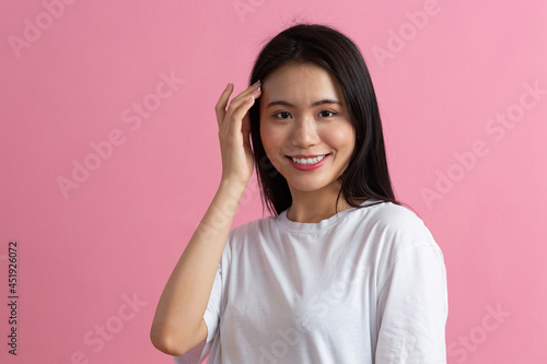 Portrait of asian positive smiling woman with hand on face on pink background.