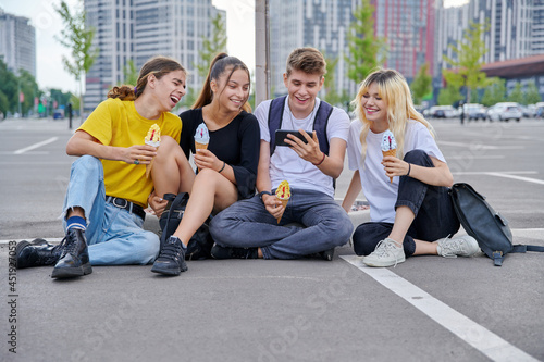 Group of teenagers with ice cream looking together at smartphone, urban style