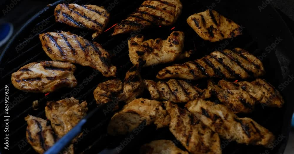 Chicken being grilled on electric grill with charred meat and red heating element burner, being flipped by hand with red painted fingernails, and tong grabber. In Cinema 4K (4096x2160) 30fps. Chicken being grilled on electric grill with charred meat and red heating element burner, being flipped by hand with red painted fingernails, and tong grabber. In Cinema 4K (4096x2160) 30fps.