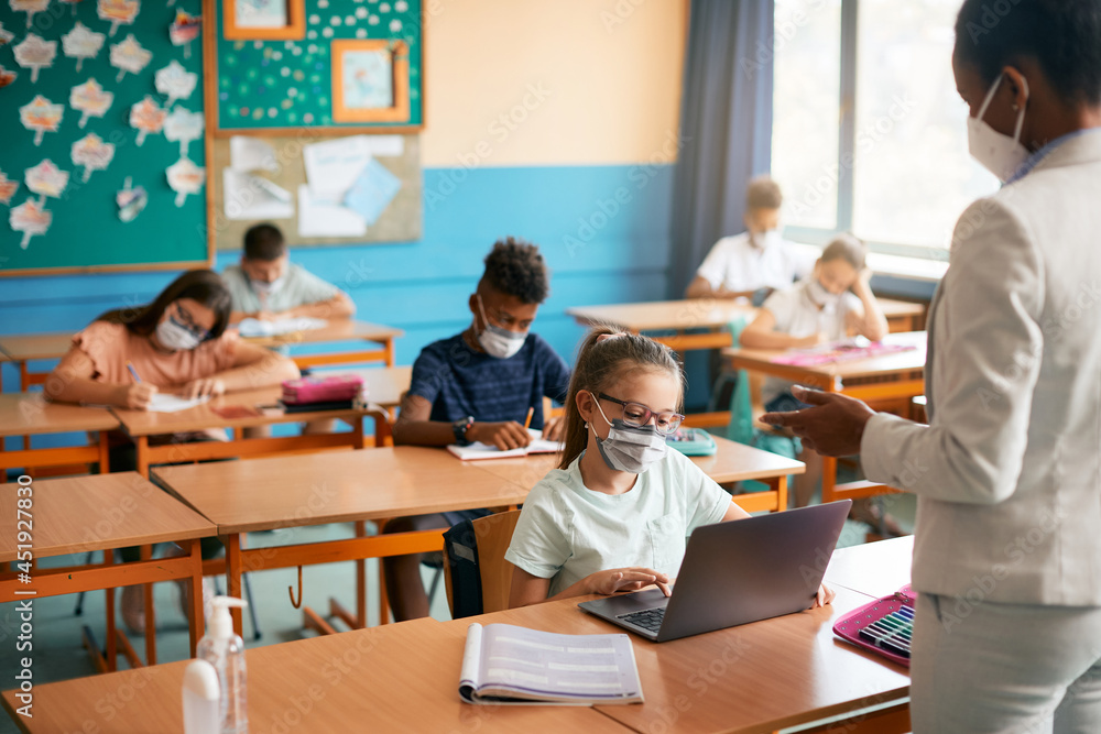 Schoolgirl wears face mask while e-learning on laptop during computer class in classroom. Schoolgirl wears face mask while e-learning on laptop during computer class in classroom.