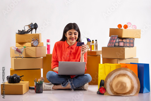 A young woman making online payment with laptop and credit card amidst shopping items in the background. photo